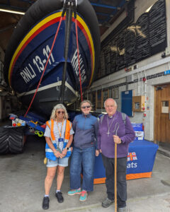 Three people stood in front of the bow of a boat inside a boat house.