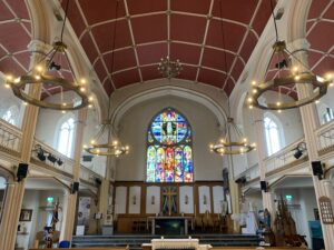 Image shows the halo heaters in the church with the stained glass window at the end and the arched roof.