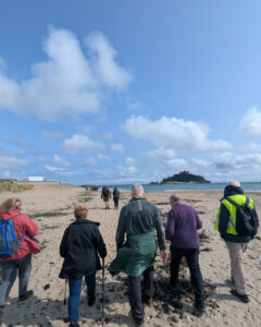 People walking away from the camera on the beach towards St Michael's Mount.