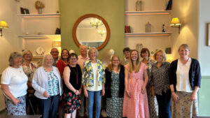Image shows a group of people looking at the camera with shelves in the background and a large circular mirror on the wall in the centre.