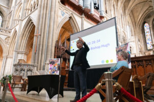 Image shows Bishop Hugh in cathedral with a screen behind him.