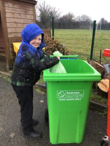 Image shows a child putting a bag in a green wheelie bin.