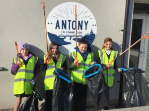 Image shows pupils in hi-vis tops with bins and litter pickers outside the sign for their school.