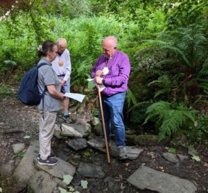 Bishop David Williams and 2 others on the walk with a stony path and shrubbery in the background.