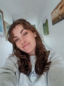 Image shows Hannah looking at the camera with paintings on the wall behind her.