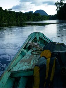Image shows the end of a boat looking out on a river with hills on the horizon.