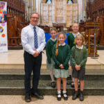 A teacher and four pupils dressed in green in the cathedral.