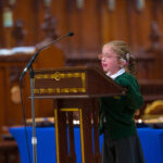 A child in green reading from the pulpit in the cathedral.