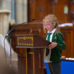 A child in green reading from the pulpit in the cathedral.