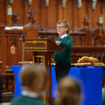 A child in green reading from the pulpit in the cathedral.