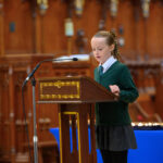 A child in green reading from the pulpit in the cathedral.