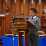 A child in grey reading from the pulpit in the cathedral.