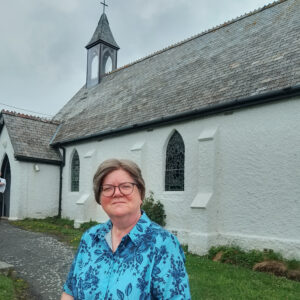 Person in blue looking at the camera with a white church-like building behind.