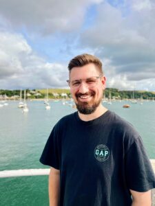 Someone looking at the camera. In the background there is water, boats and a cloudy sky.