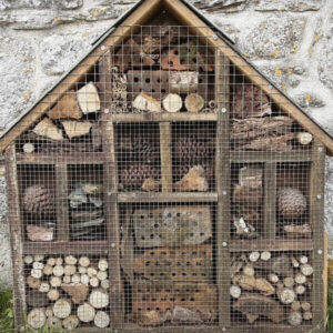 A wooden bug hotel with a number of segments with items in there such as twigs, against a brick wall