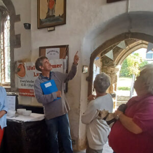 People inside the church being taken on a tour. One person is holding a blue folder and pointing while two other people are looking.