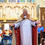 The Bishop of Truro in a church - his arms are open wide.