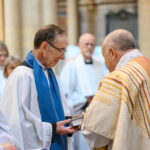 A person in white with blue and the back of the Bishop of Truro.