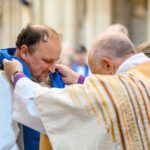 Bishop David putting cloth around a person's shoulders.