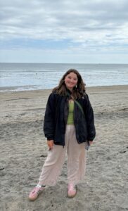 Rosie is stood on the beach with a cloudy sky and the sea in the background.