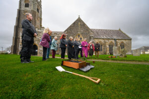 People gathered outside a church with a spade in the foreground.