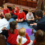 Children sat in a circle on the floor around an adult leading a workshop.