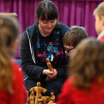 An adult showing children wooden figures.