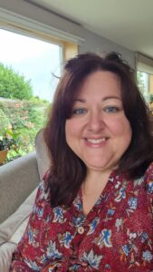 Image shows Rebecca smiling at the camera with greenery in the background.