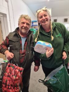 Two people looking at the camera. They are holding carrier bags and the person on the right is holding a blue and white package too.