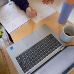 Hands writing, and a laptop and drinks.