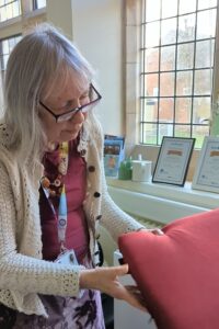 Rosey Sanders in the office holding a red, heated cushion.