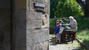 A brick wall to the left, to the right in the distance children and adults taking part in a workshop.