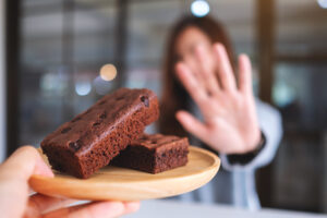 Image shows a plate with brownies on a plate and a person in the background with their hand palm forward as if saying 'no'.