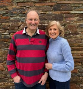 Andrew and Sally looking at the camera - a brick wall is behind them.