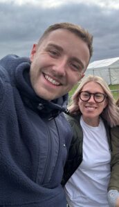 Two people smiling at the camera and a tent and cloudy sky in the background.