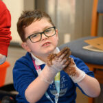 A child with muddy hands looking at the camera.