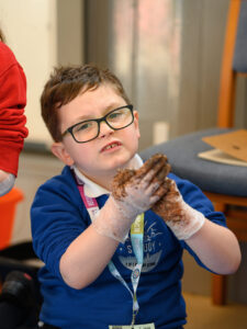 A child with muddy hands looking at the camera.