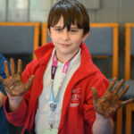 A child with muddy hands looking at the camera.