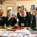Children showing off their artwork. The table in front is full of the creative materials.