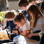 Children taking part in a workshop. A watering can sits on the table
