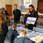 A person holding an illustration board whilst talking to children.