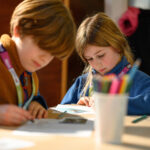Two children working with a blurred pencil pot in the foreground.