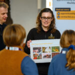 A person holding an illustration board whilst talking to children.
