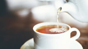 A white teapot pouring tea into a white cup with saucer.