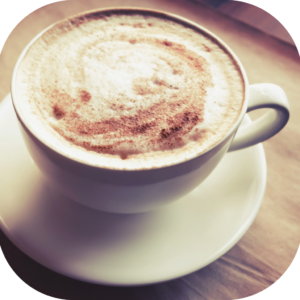 A cup of coffee with chocolate sprinkled on top of steamed milk. It sits on a wooden surface.