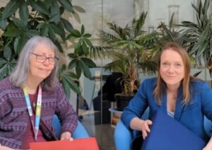 Two people holding a heated cushion with plants in the background