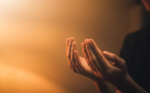 Open hands praying with an orange/brown background.