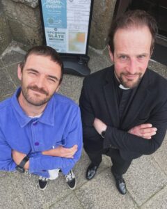 Two people stood with arms crossed and a notice board behind them